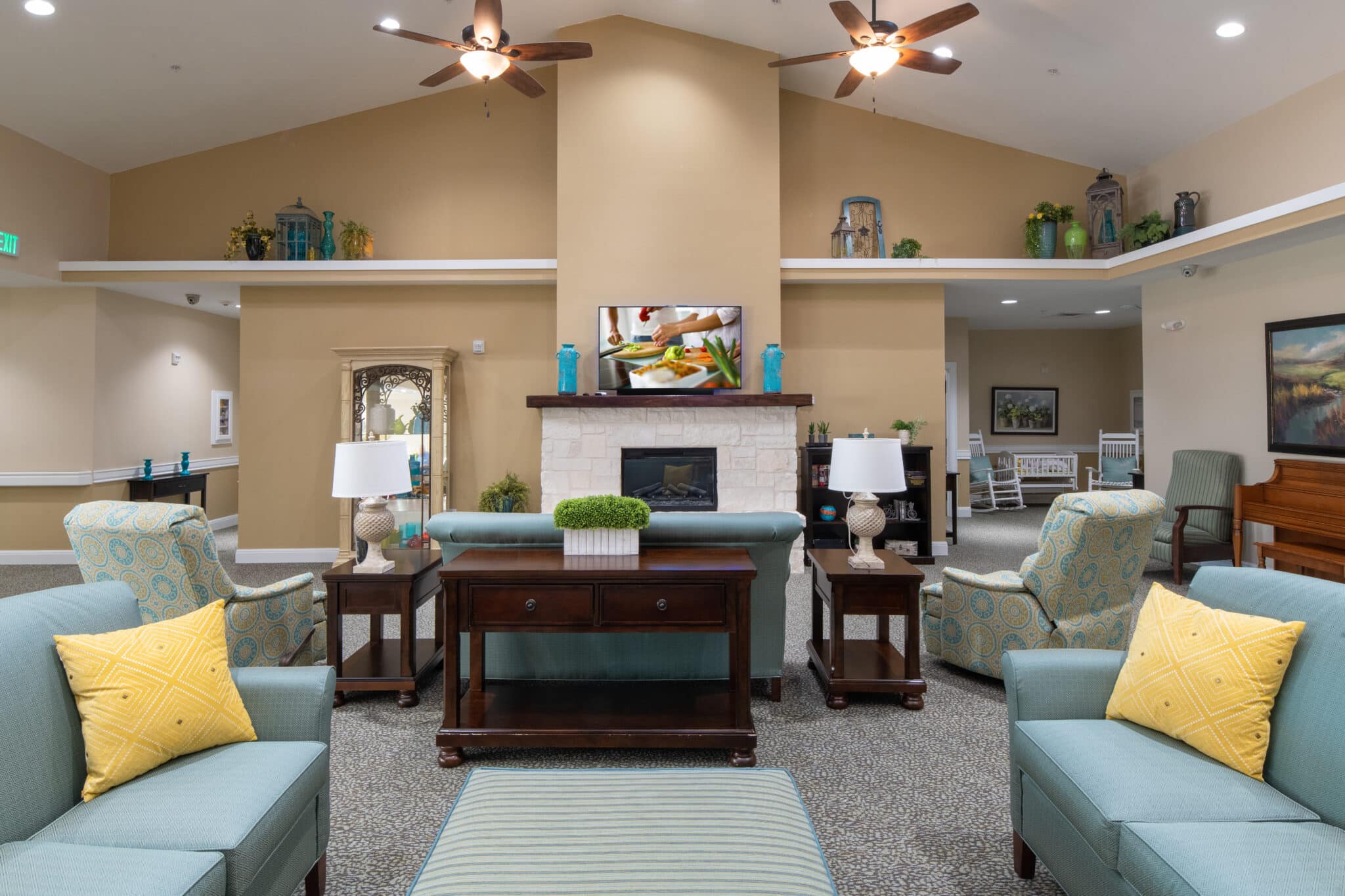 Cozy lounge area in assisted living facility with seating, fireplace, piano, and TV.