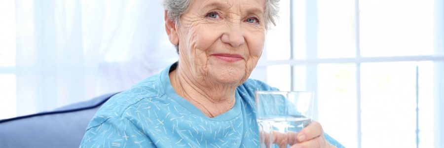 Elderly,Woman,Sitting,On,Couch,And,Holding,Glass,Of,Water.